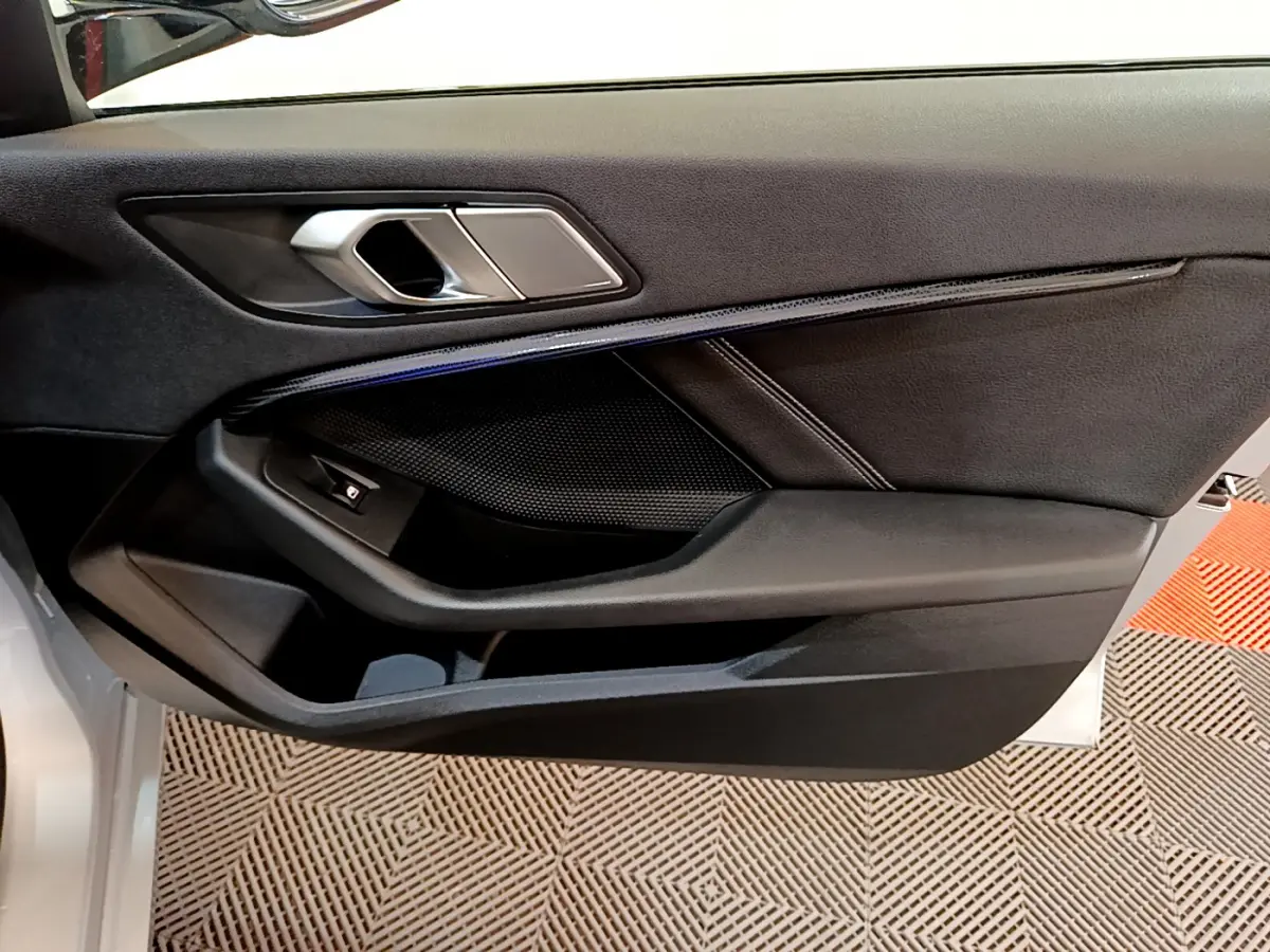 Intérieur côté gauche de la porte BMW Série 1 gris clair, avec poignée argentée et garniture noire élégante.