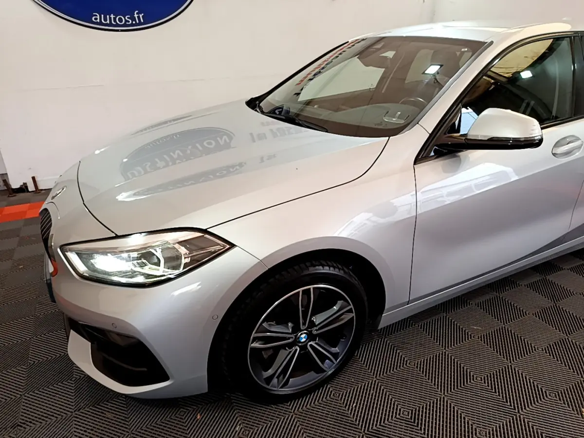 BMW Série 1 gris clair vue 3/4 avant droit avec phares LED allumés et jantes alliage sport