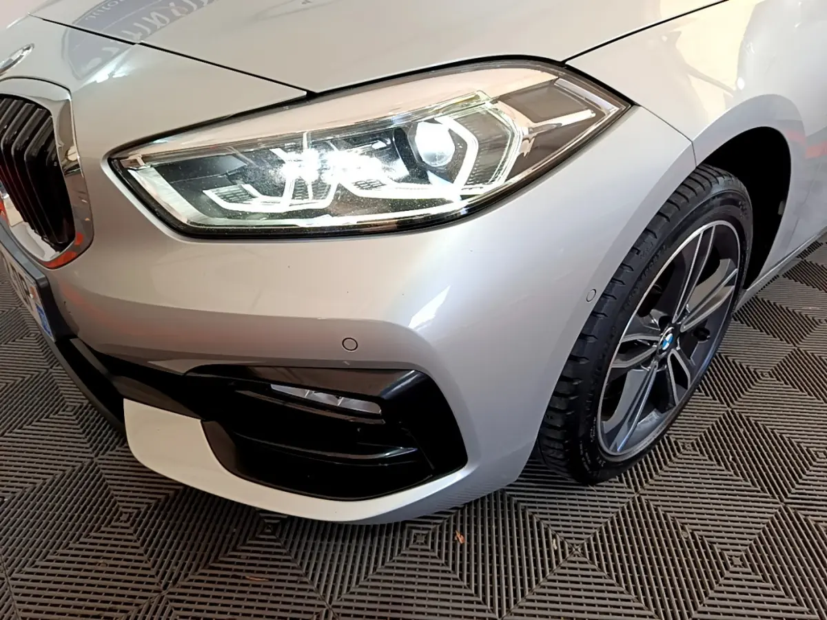 Gros plan sur l'avant droit d'une BMW Série 1 gris clair, mettant en valeur le phare LED et la jante alliage.