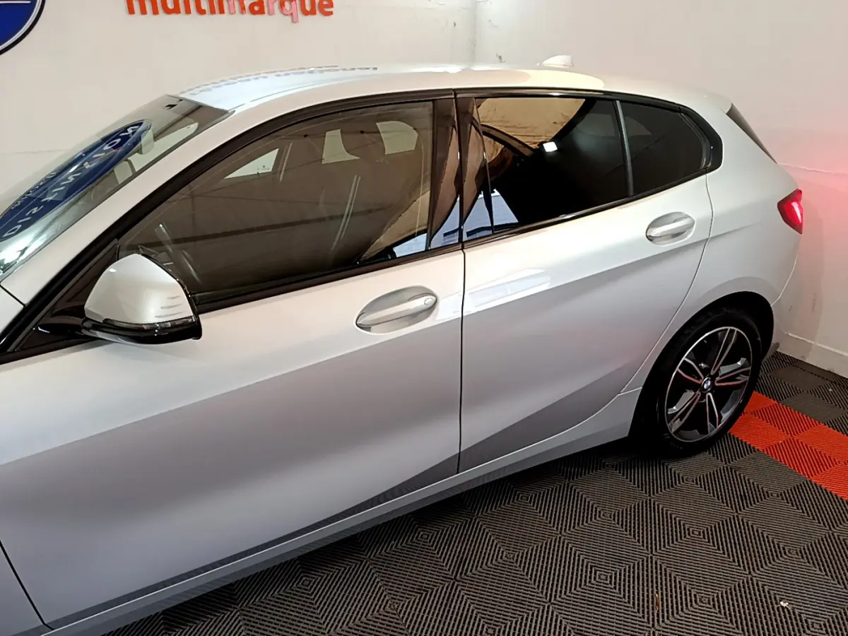 Vue latérale côté gauche d'une BMW Série 1 gris clair avec vitres teintées et jantes alliage sport.