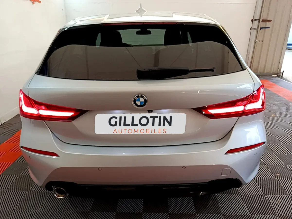 Vue arrière d'une BMW Série 1 gris clair de 2021 avec feux LED allumés et plaque GILLOTIN Automobiles.