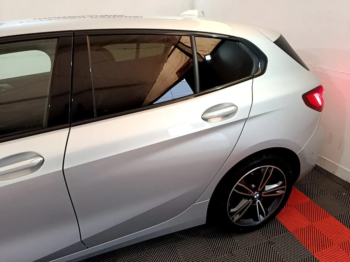 Vue côté droit arrière d'une BMW Série 1 gris clair avec jante alliage et feux arrière allumés dans un garage.