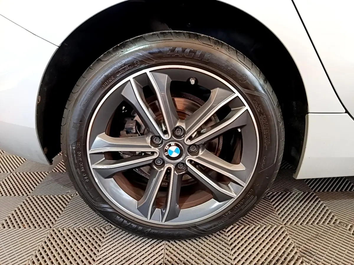 Gros plan sur la roue avant droite d'une BMW Série 1 gris clair avec jante alliage à 5 doubles branches.