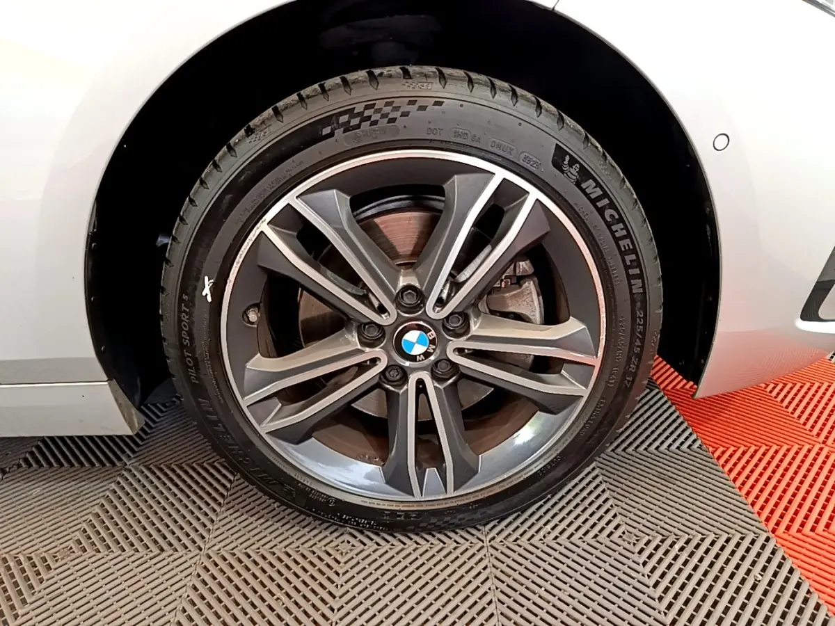 Gros plan sur la roue avant droite avec jante alliage gris et logo BMW sur une BMW Série 1 gris clair.