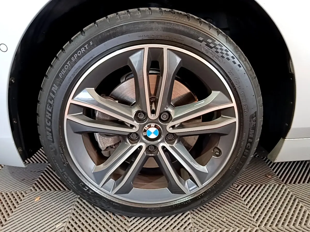 Gros plan sur la roue avant droite gris clair d'une BMW Série 1 118i Edition Sport avec jante alliage et logo BMW central.