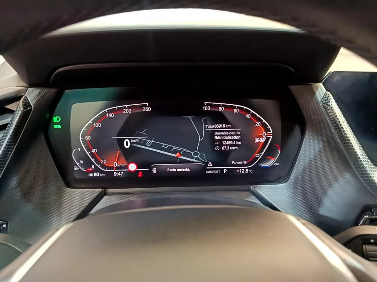 Vue rapprochée du tableau de bord numérique de la BMW Série 1 gris clair avec affichage multifonctions et indicateurs rouges.