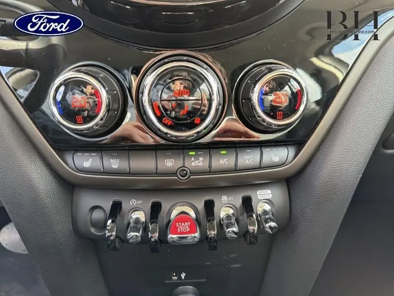 Gros plan sur la console centrale noire brillante de la MINI Countryman 2023 avec commandes de climatisation et bouton Start/Stop rouge.