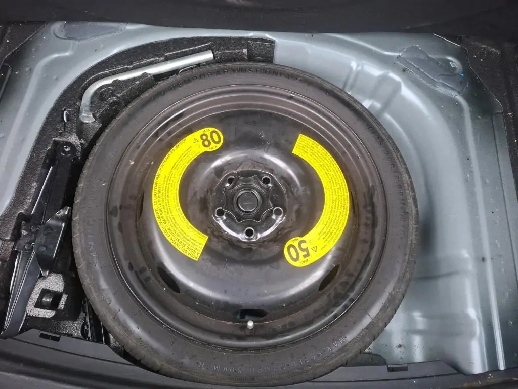 Vue rapprochée de la roue de secours noire avec étiquettes jaunes dans le coffre d’une SEAT Leon gris 2021.