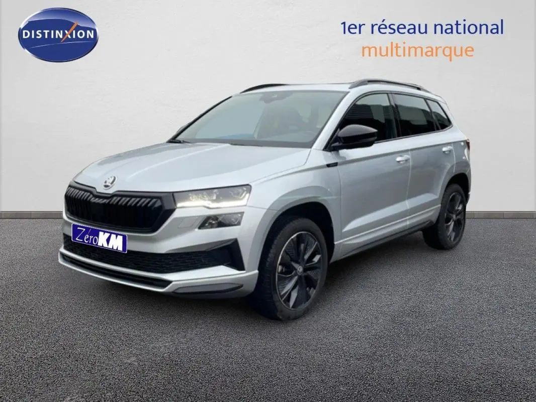 Vue 3/4 avant d'un Skoda Karoq argent 2025 avec barres de toit et jantes noires sur fond neutre.