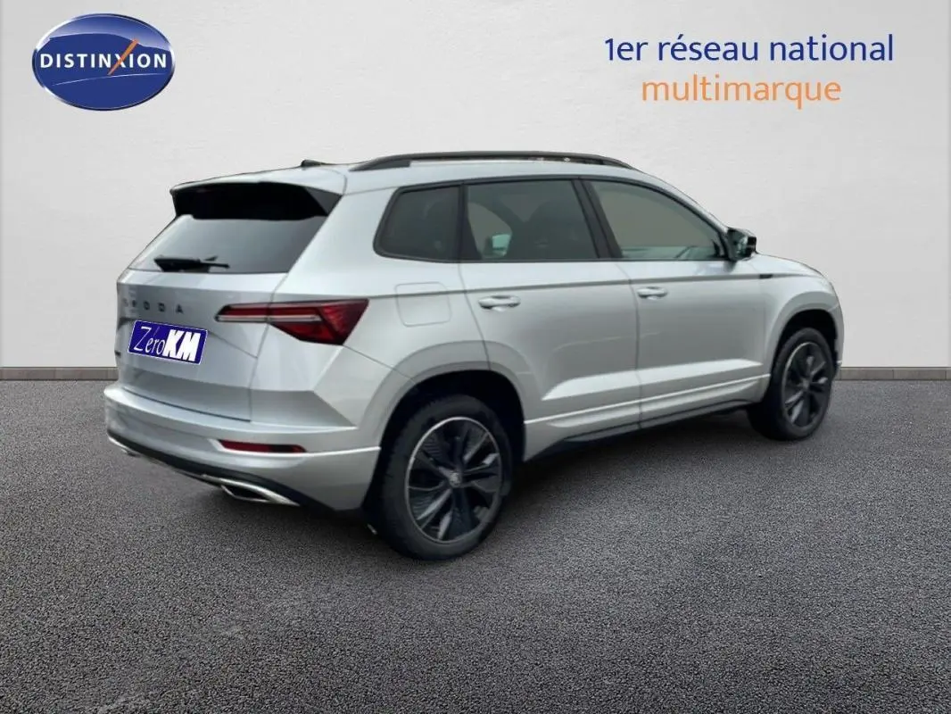 Vue 3/4 arrière droite d'un Skoda Karoq argent 2025 avec barres de toit et vitres teintées.