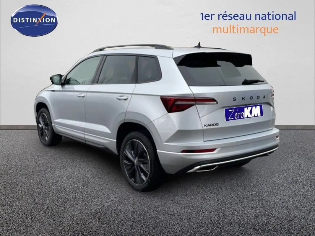 Vue 3/4 arrière droite d'un Skoda Karoq argent 2025 avec barres de toit et vitres teintées.