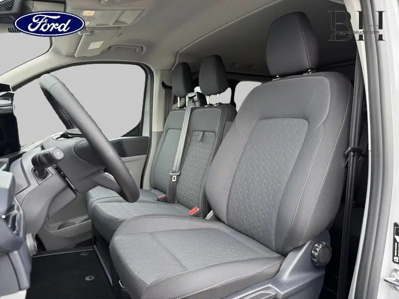 Vue intérieure côté conducteur du Ford Transit Custom Fourgon 2026, sièges gris avec ceinture de sécurité visible.