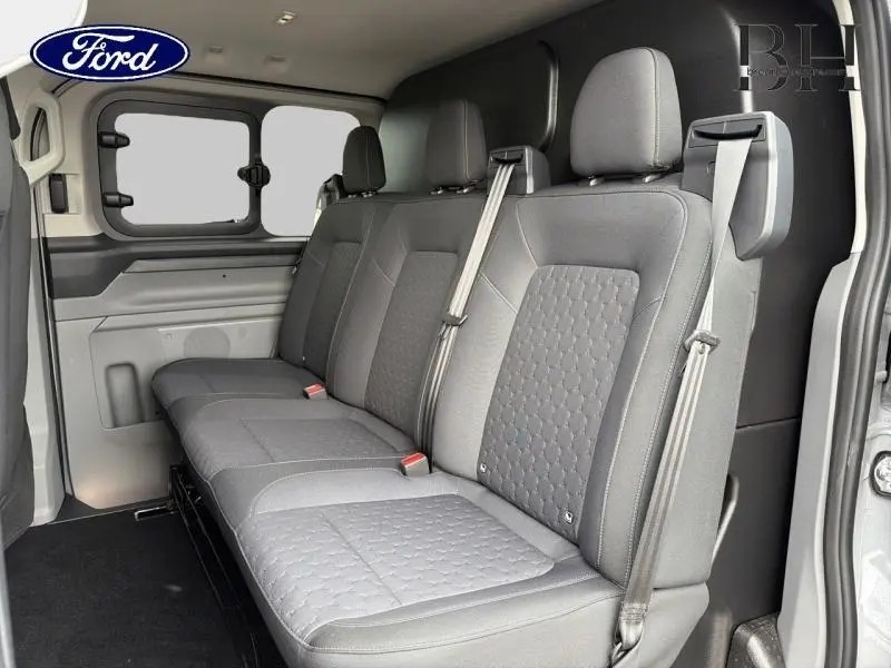 Vue intérieure côté droit sur la banquette arrière grise du Ford Transit Custom Fourgon 2026 avec vitres latérales entrebaillantes.