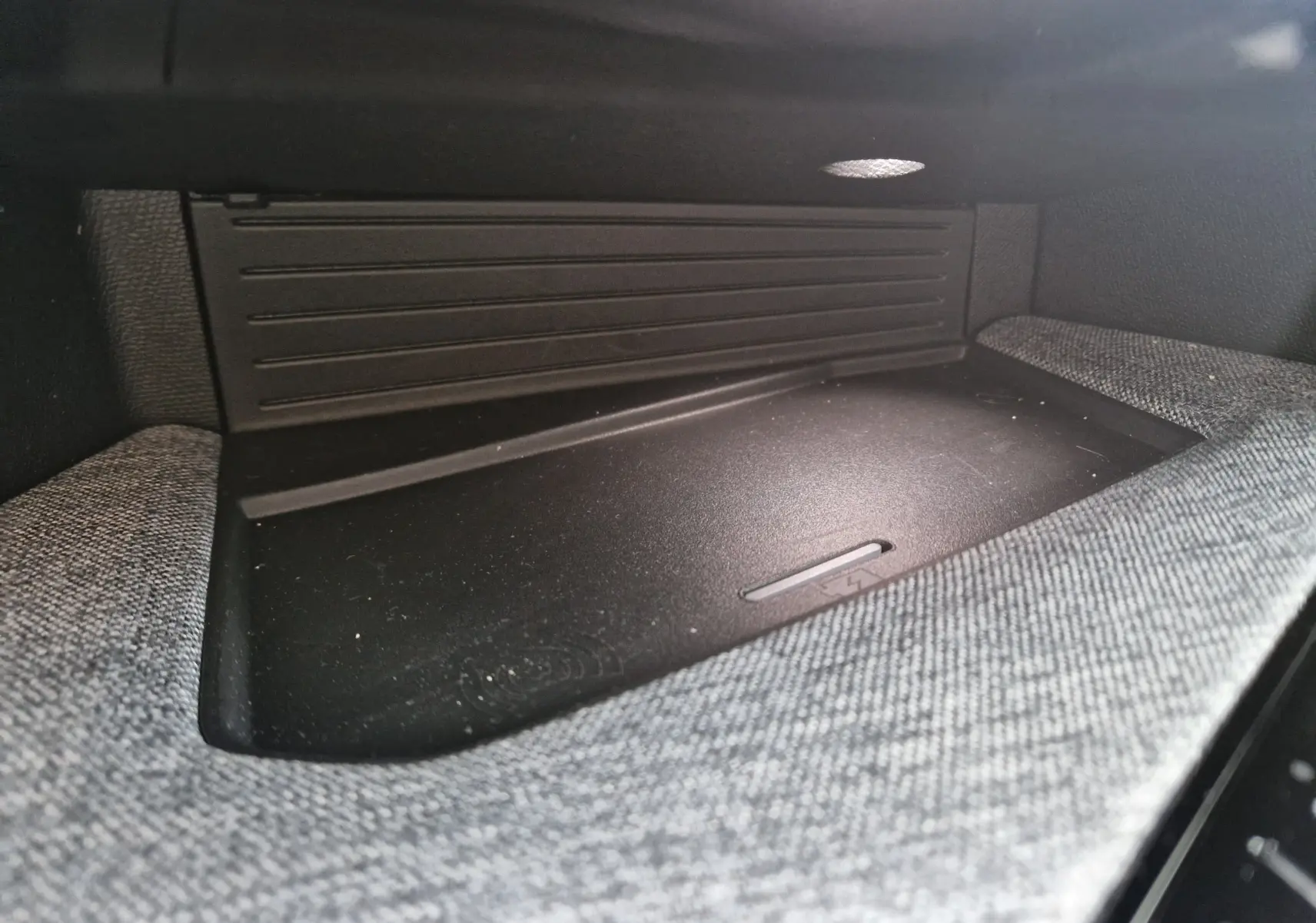 Gros plan sur le compartiment de rangement intérieur avec surface de charge sans fil, tissu gris et plastique noir dans un Peugeot 3008.