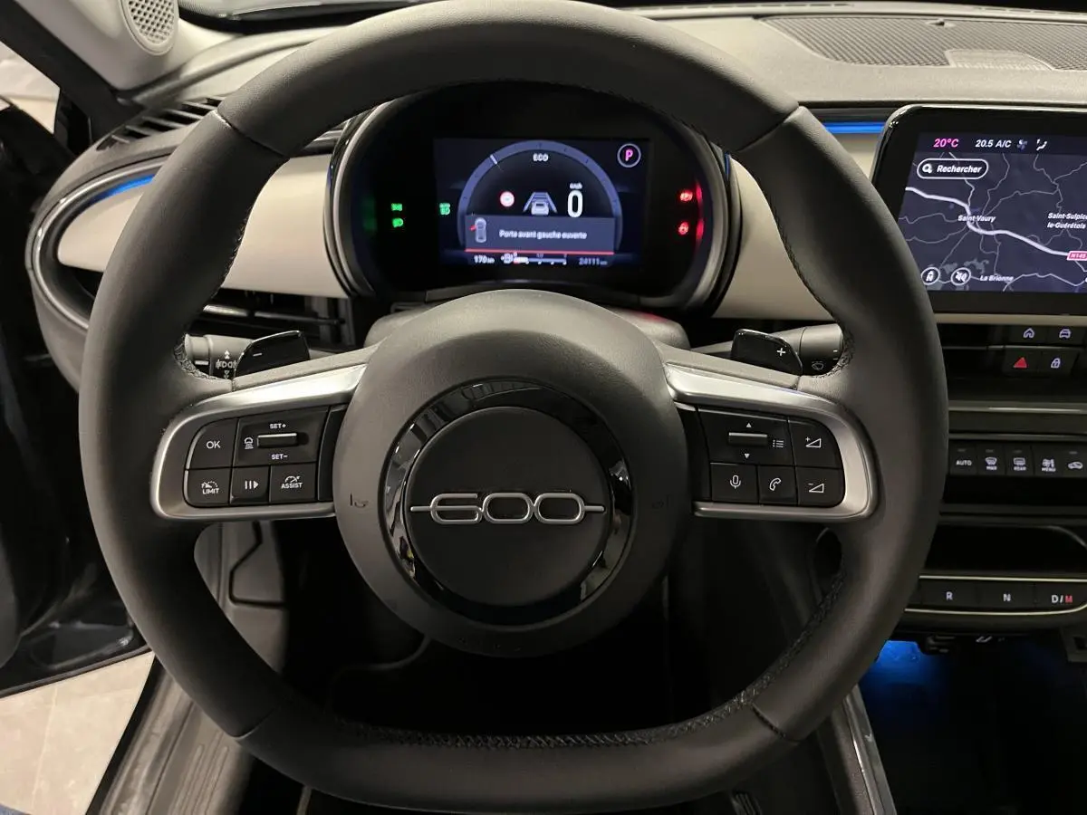 Vue rapprochée du volant noir du Fiat 600 1.2 Hybrid 2024 avec commandes intégrées et tableau de bord numérique.