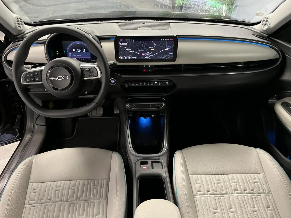 Intérieur de la FIAT 600 hybride 2024 vu de face, avec sellerie ivoire et tableau de bord moderne éclairé bleu.