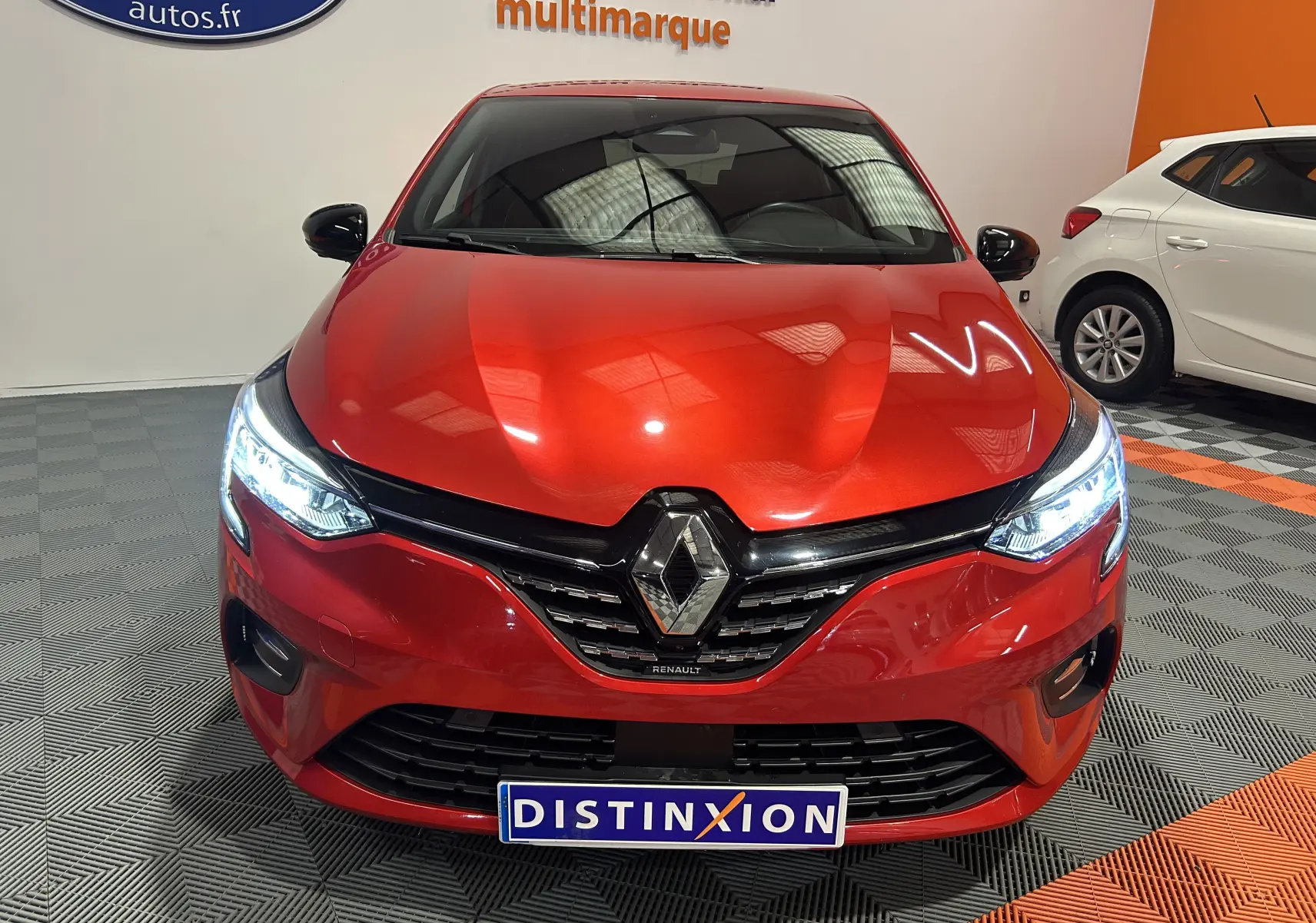 Vue frontale d'une Renault Clio V TCe 90 TECHNO rouge avec phares LED allumés en intérieur showroom.