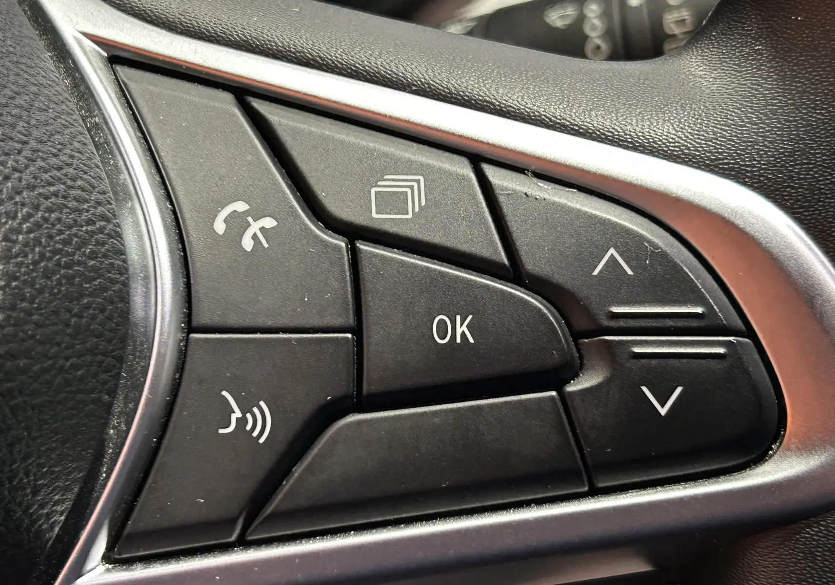 Gros plan sur les commandes noires du volant de la Renault Clio V rouge, boutons multifonctions avec cadre argenté.