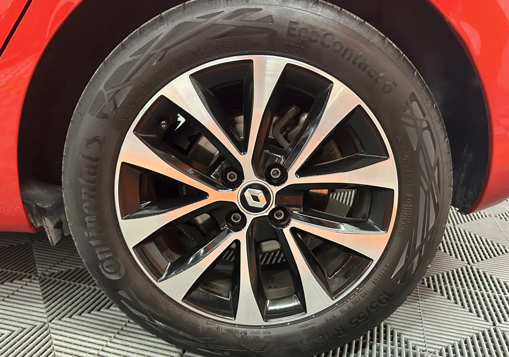 Gros plan sur la roue avant gauche de la Renault Clio V rouge, jante alliage bicolore avec logo Renault central.