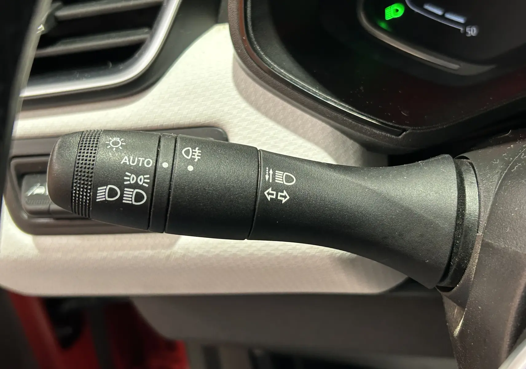 Gros plan sur la commande des feux et clignotants à gauche du volant dans l'habitacle d'une Renault Clio V rouge.