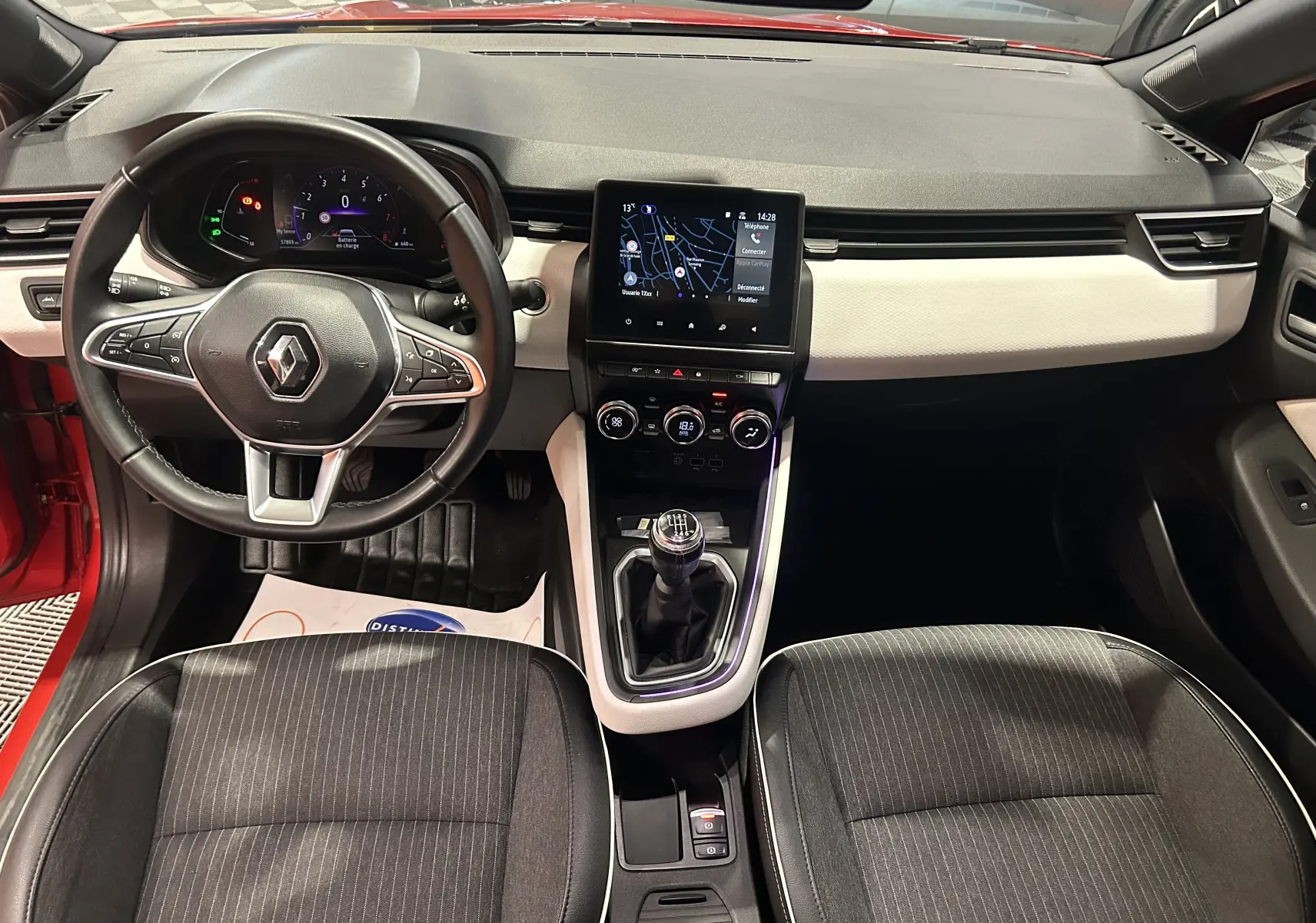 Vue intérieure avant de la Renault Clio V TCe 90 TECHNO rouge 2023, avec tableau de bord clair et levier de vitesse manuel.