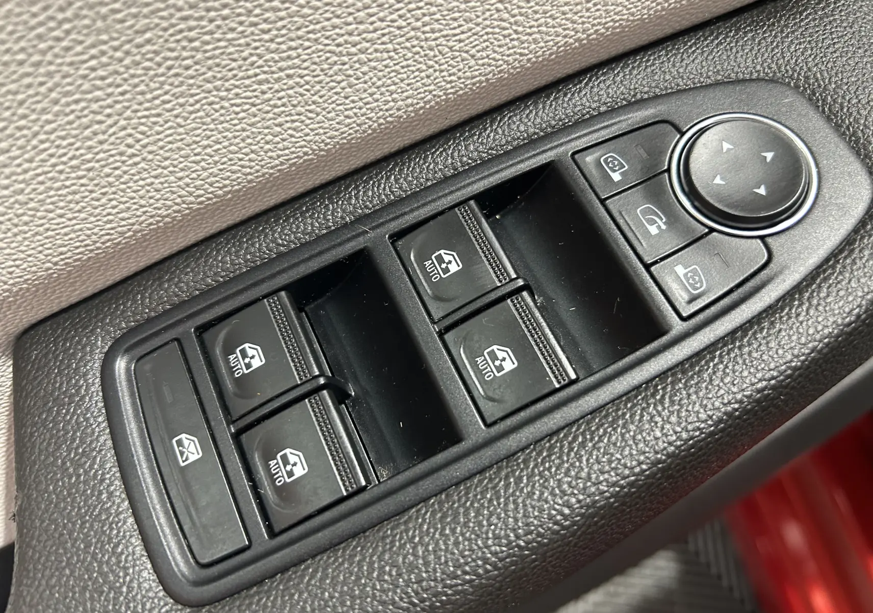 Gros plan sur les commandes de lève-vitres et réglage des rétroviseurs côté gauche d'une Renault Clio V rouge 2023.