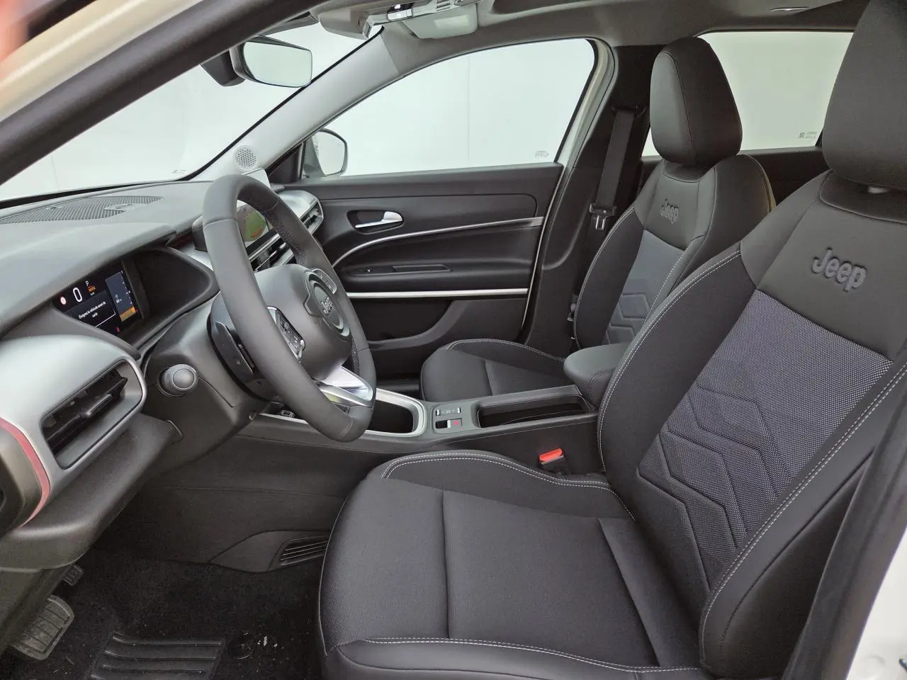 Vue intérieure côté conducteur du Jeep Avenger 2025, sièges noirs avec logo Jeep brodé et tableau de bord moderne.