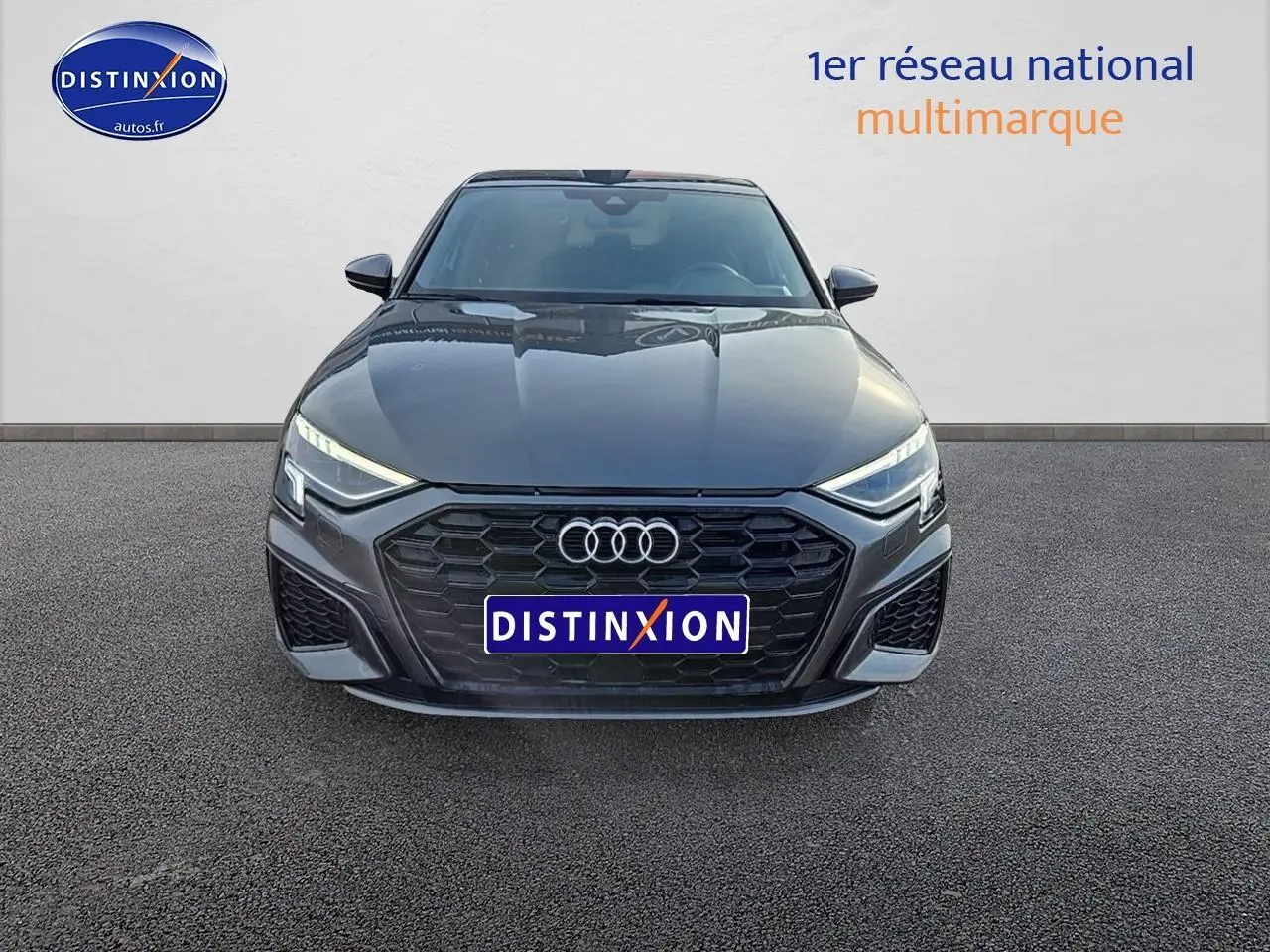Vue frontale d'une Audi A3 Sportback gris Daytona avec calandre noire et phares LED allumés.