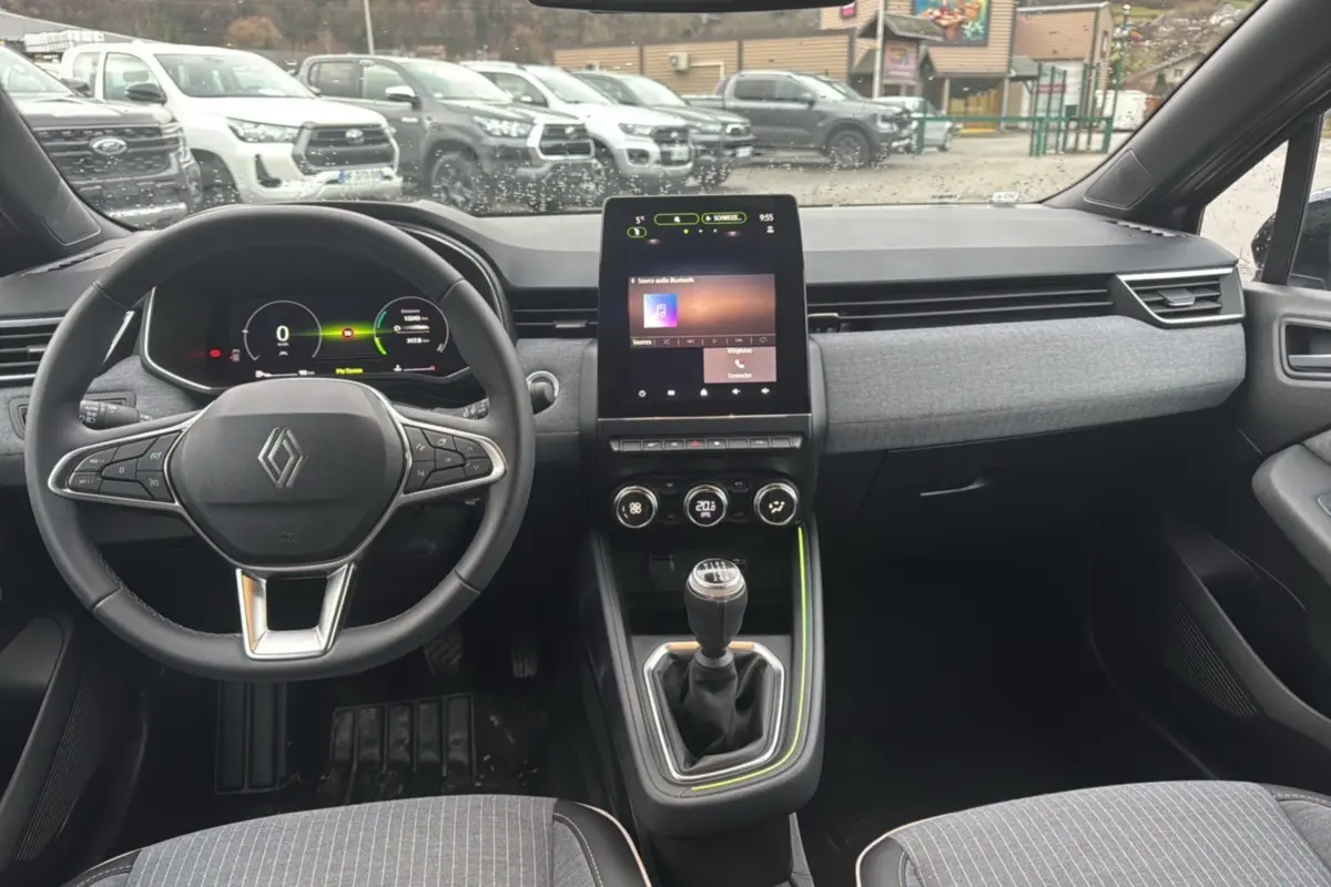 Vue intérieure avant de la Renault Clio V TCE 90 Techno Plus 2025, tableau de bord gris avec écran tactile vertical et boîte manuelle.