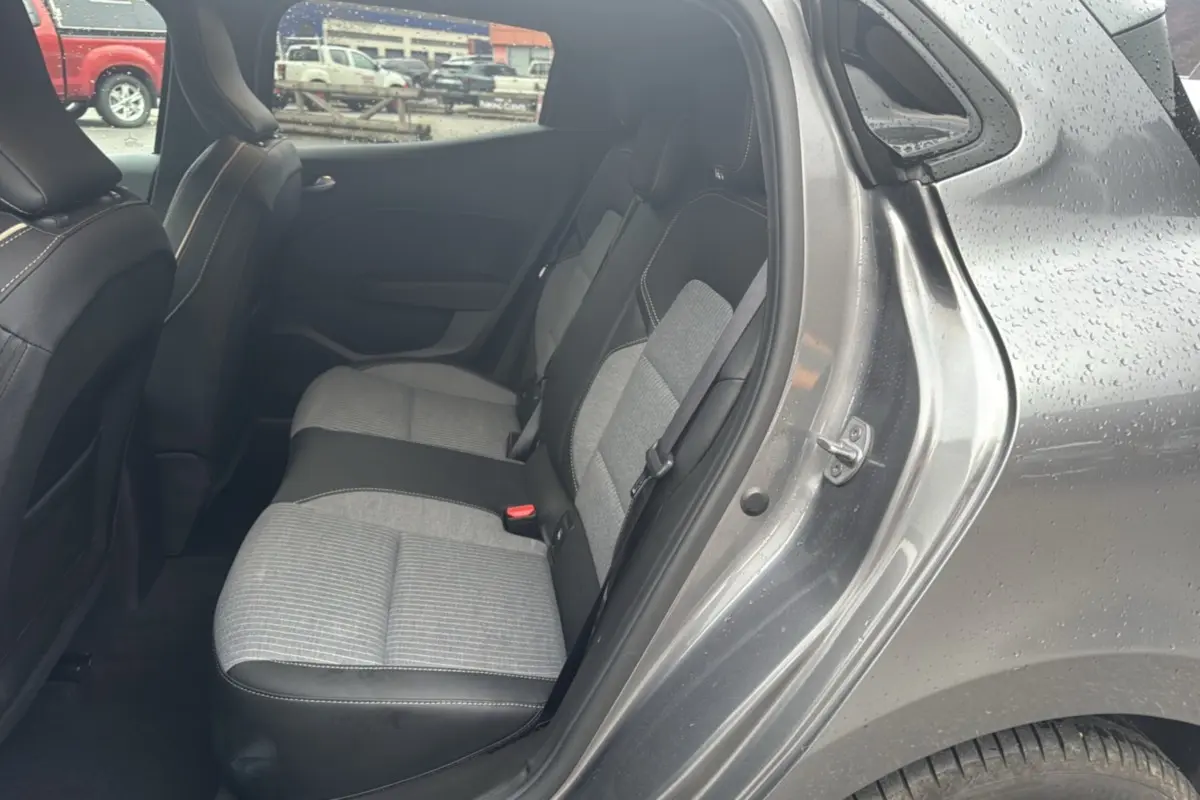 Vue côté droit sur la banquette arrière gris clair et noir de la Renault Clio gris schiste 2025 avec portière ouverte sous la pluie.
