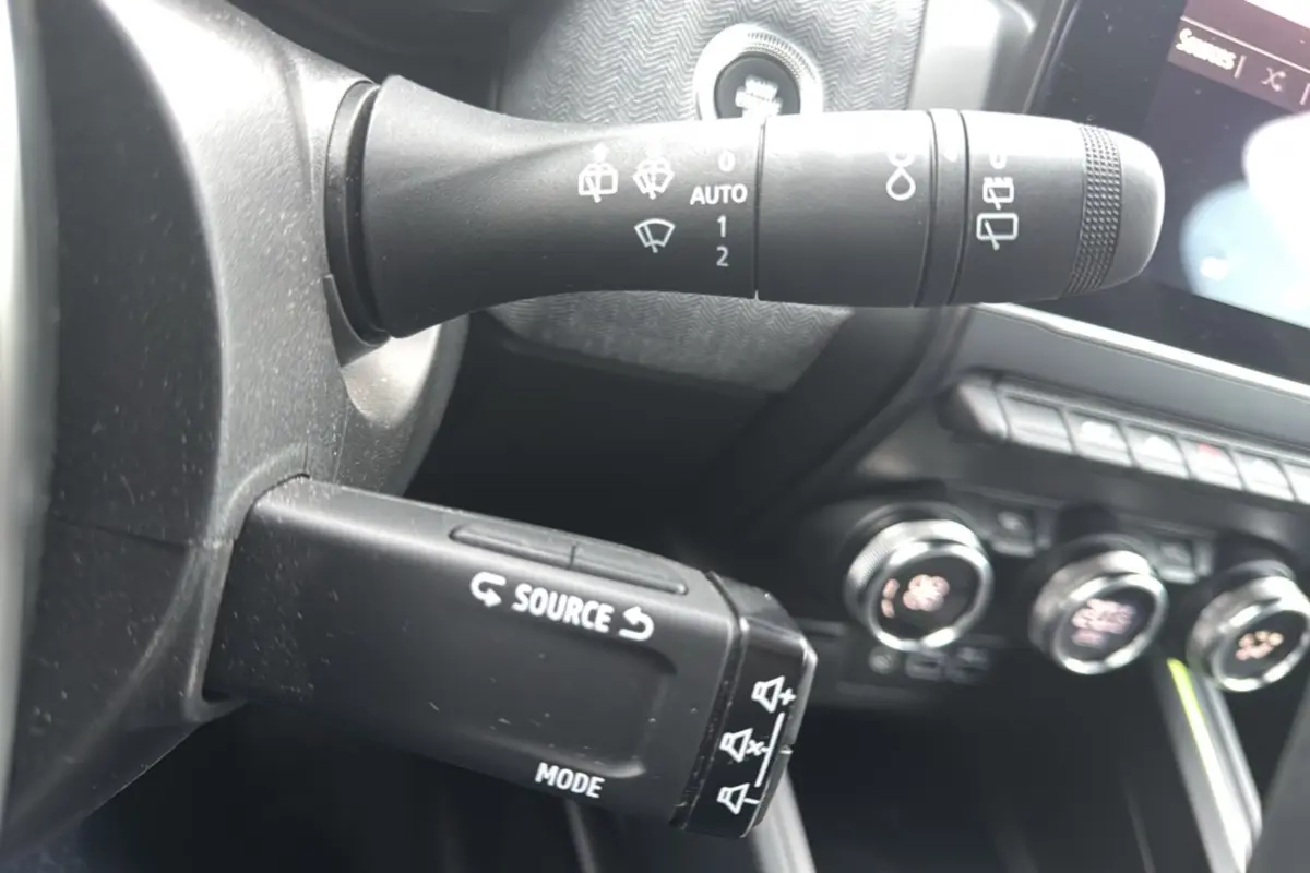 Gros plan sur la commande multifonction gauche du volant de la Renault Clio gris schiste, avec tableau de bord et commandes clim visibles.