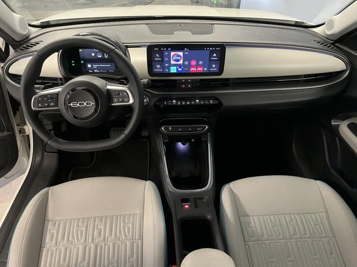 Vue intérieure avant du tableau de bord ivoire et volant noir marqué 600, sièges ivoire avec monogrammes FIAT visibles.