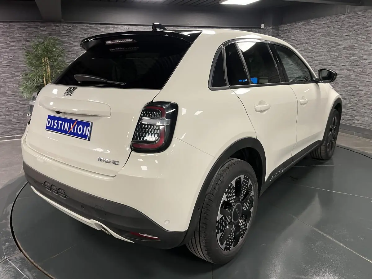 Vue 3/4 arrière droite d'une FIAT 600 blanche hybride 2024 avec jantes alliage noires et toit noir brillant.