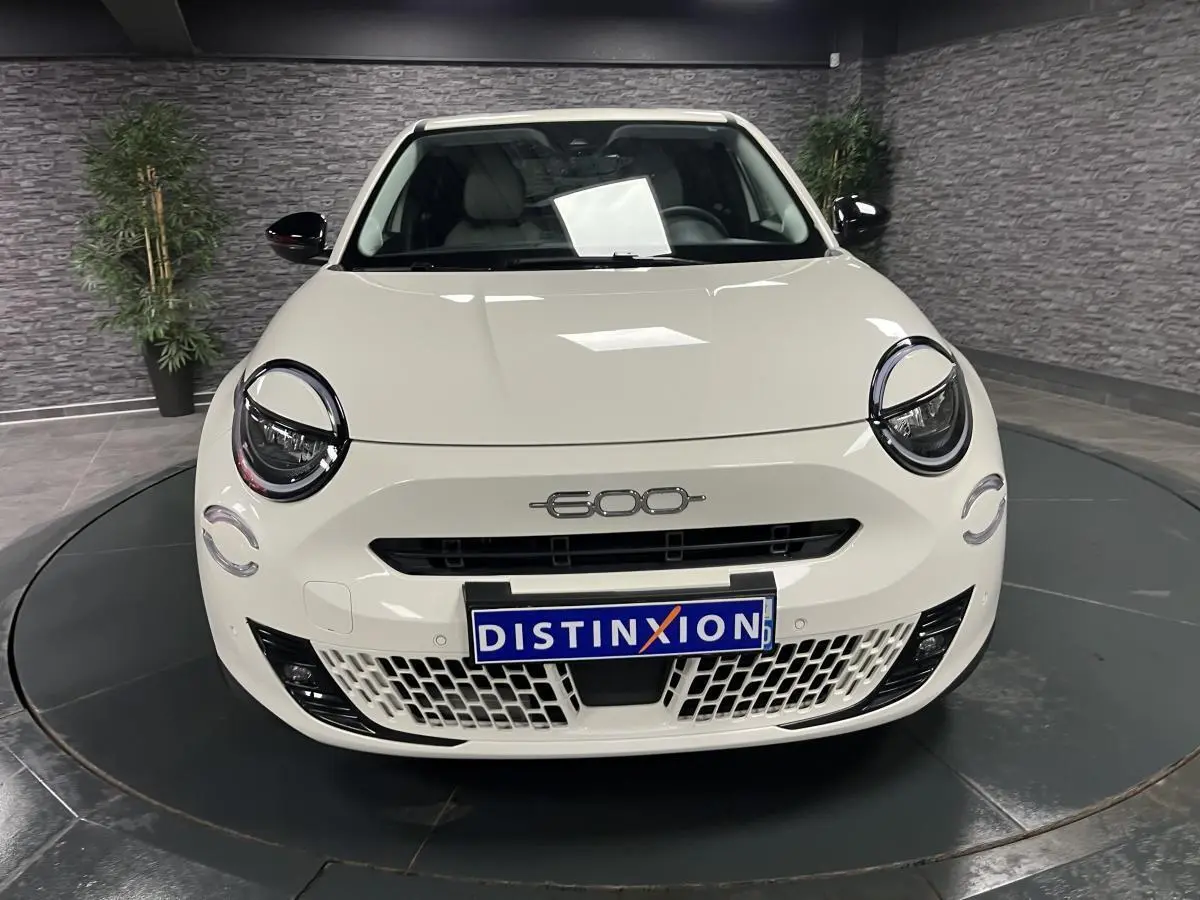 Vue frontale d'une FIAT 600 blanche avec logo chromé 600 et calandre ajourée dans un showroom.