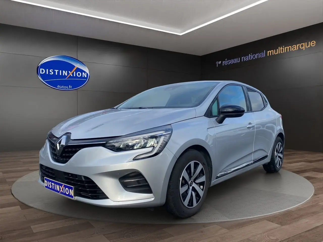 Renault Clio V TCE 90 Evolution gris Highland vue 3/4 avant droit avec vitres arrière surteintées et jantes spécifiques.