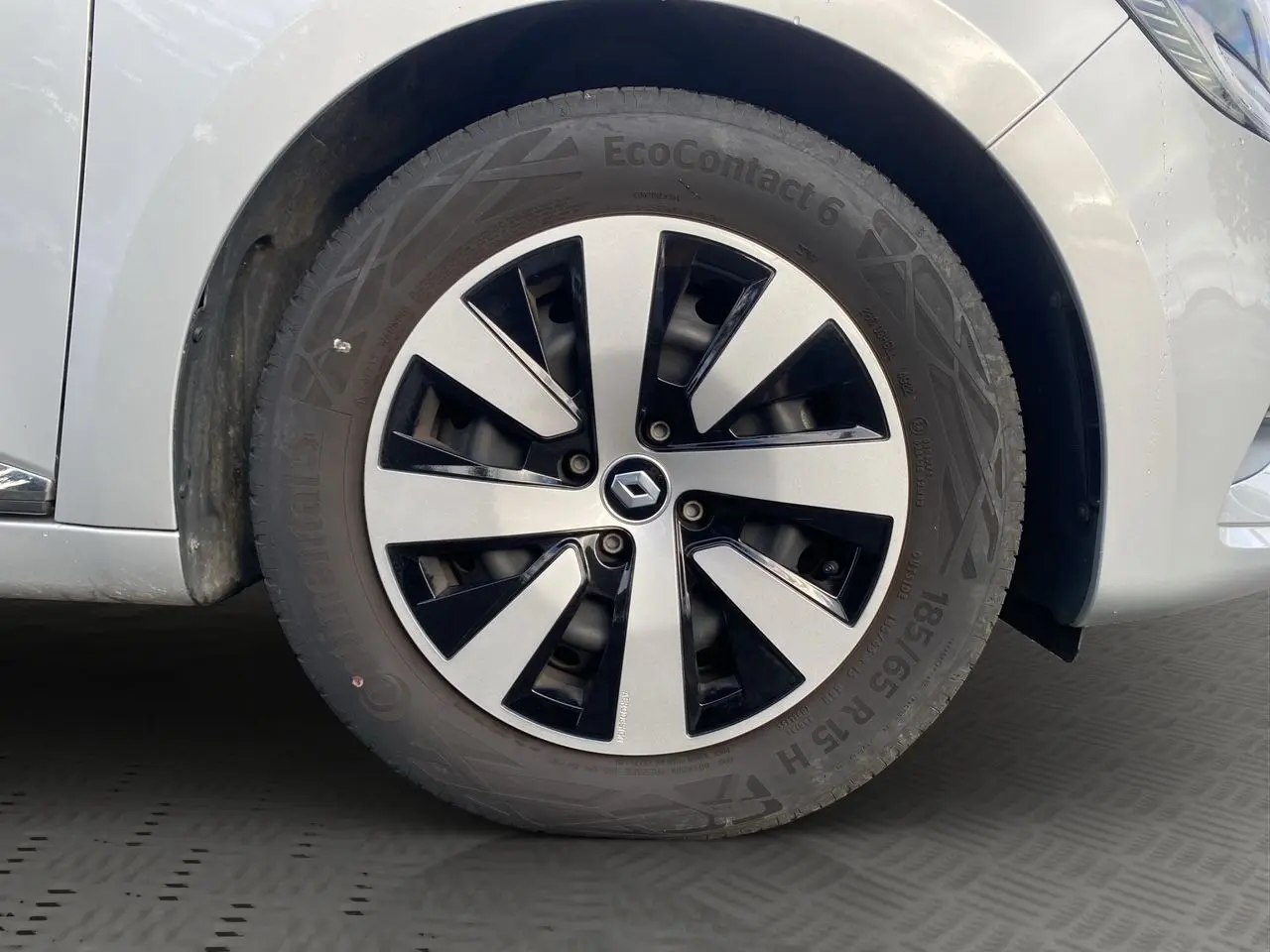 Gros plan sur la roue avant droite de la Renault Clio V gris Highland avec jante alliage bicolore et logo Renault central.