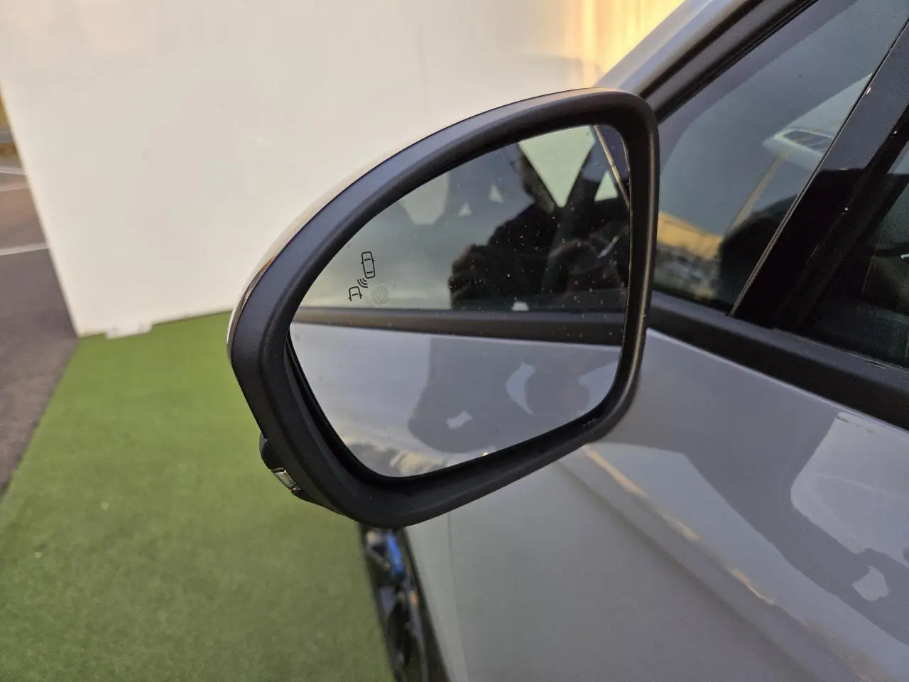 Rétroviseur côté gauche de la Renault Clio V hybride gris Rafale avec indicateur d'angle mort visible.