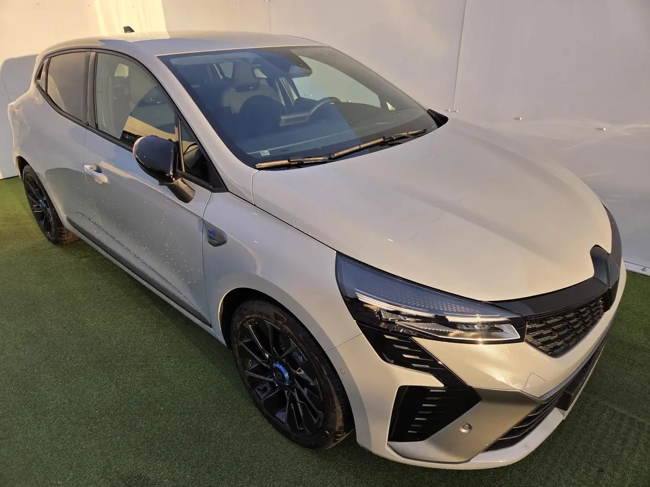 Renault Clio V hybride gris Rafale vue 3/4 avant gauche avec jantes noires et rétroviseurs noirs brillants.