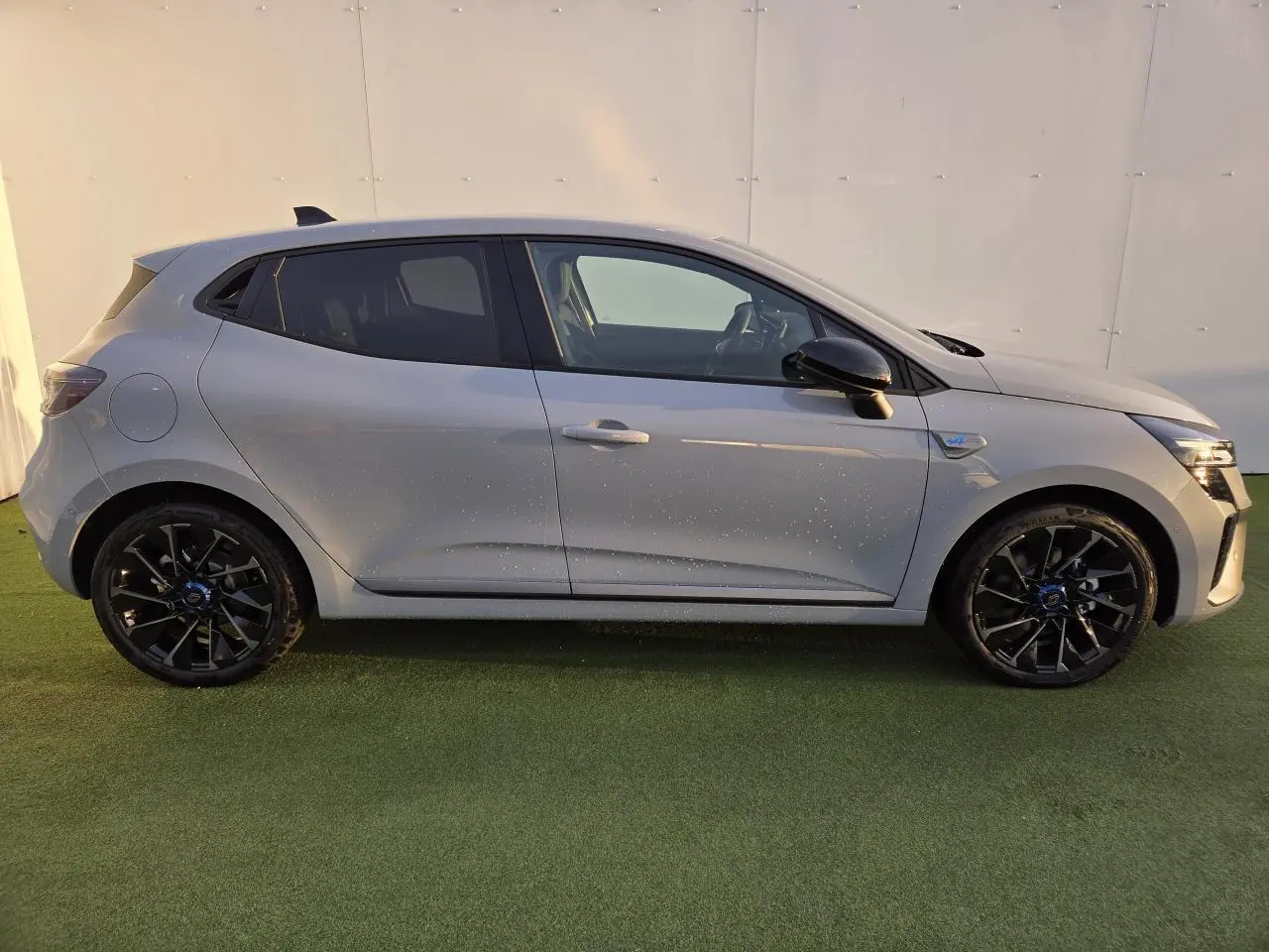 Profil droit d'une Renault Clio V hybride gris Rafale avec jantes alliage noires et rétroviseurs noirs brillants.