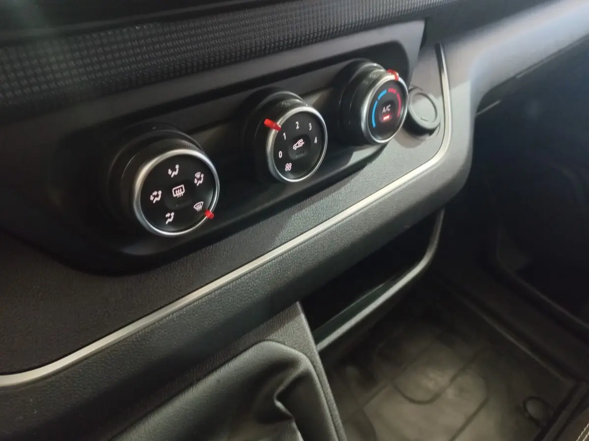 Gros plan sur les commandes de climatisation noires du tableau de bord du Renault Trafic Fourgon blanc, version 2022.