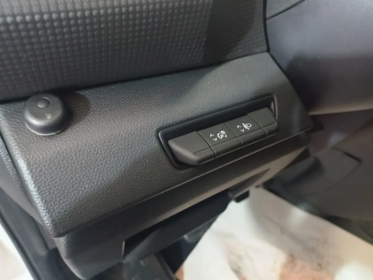 Gros plan sur les commandes de réglage manuel des phares à l'intérieur du Renault Trafic Fourgon blanc, côté conducteur.