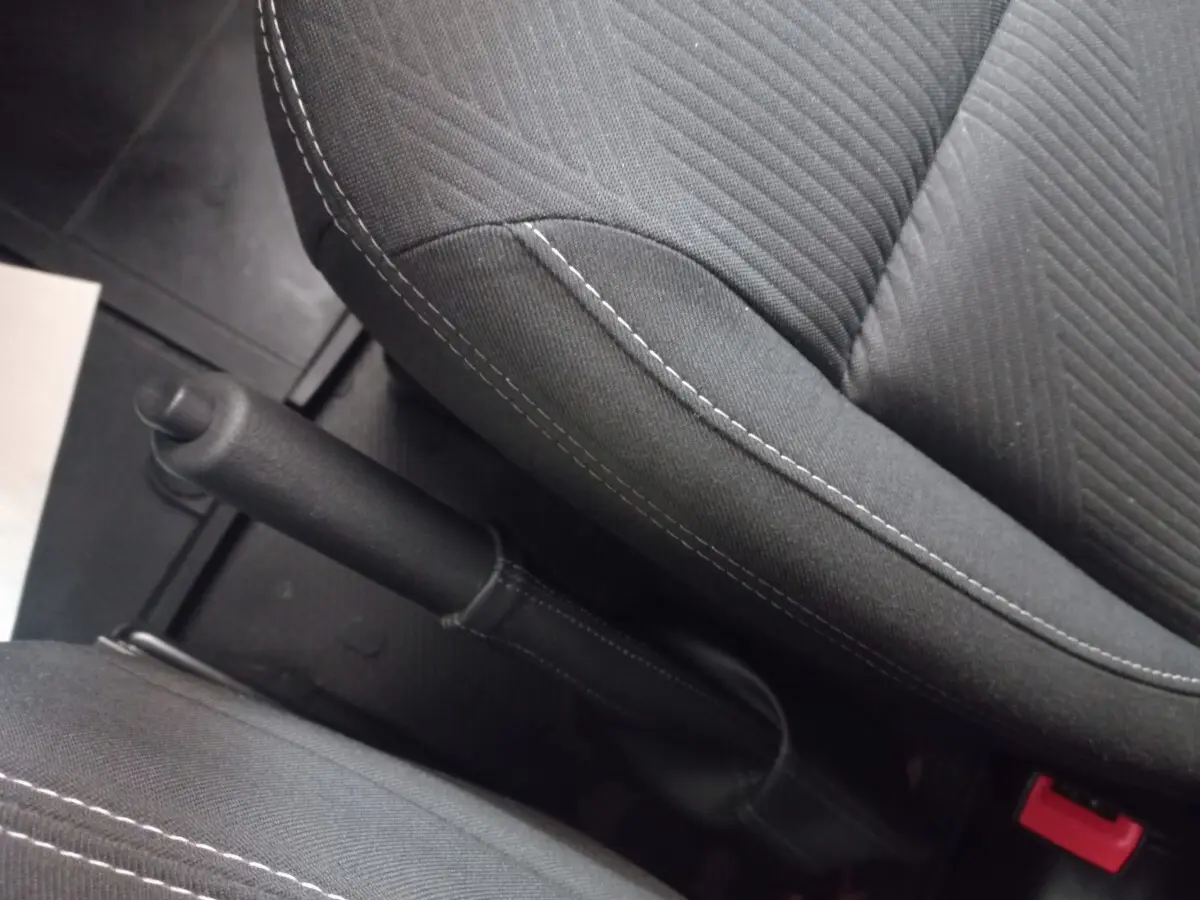 Vue rapprochée de la poignée de frein à main entre les sièges avant noirs du Renault Trafic Fourgon blanc.