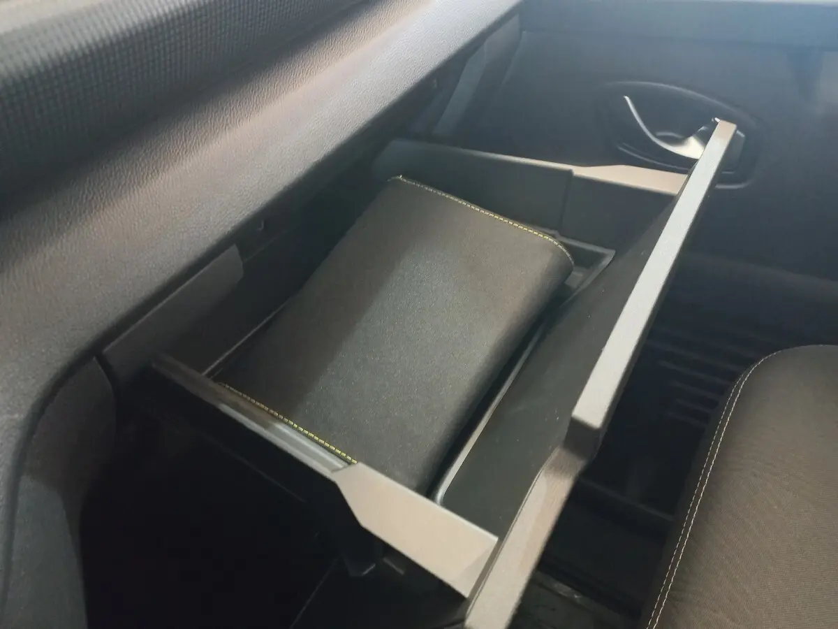 Tiroir de rangement ouvert côté passager dans l'habitacle du Renault Trafic Fourgon blanc, avec un carnet à l'intérieur.