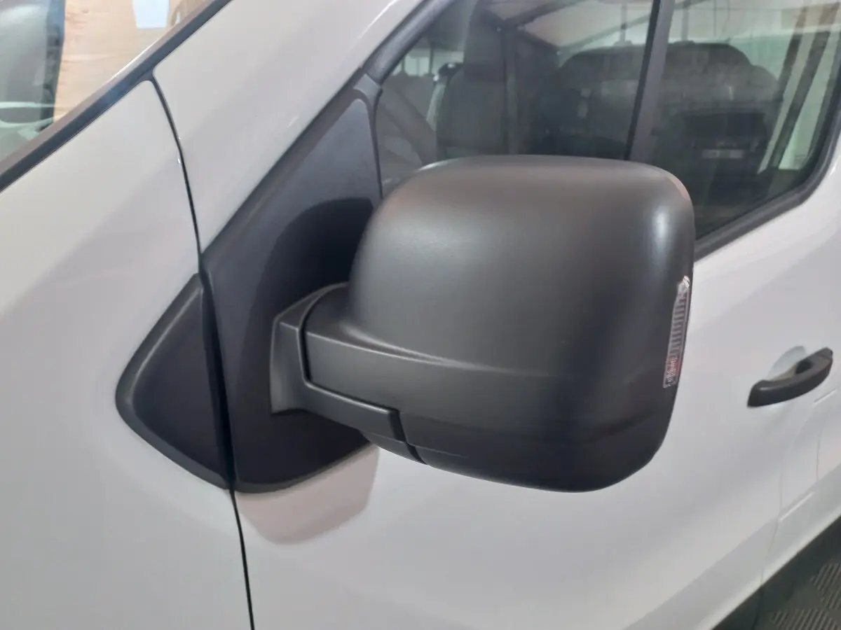 Gros plan sur le rétroviseur noir rabattable électriquement côté gauche du Renault Trafic Fourgon blanc.