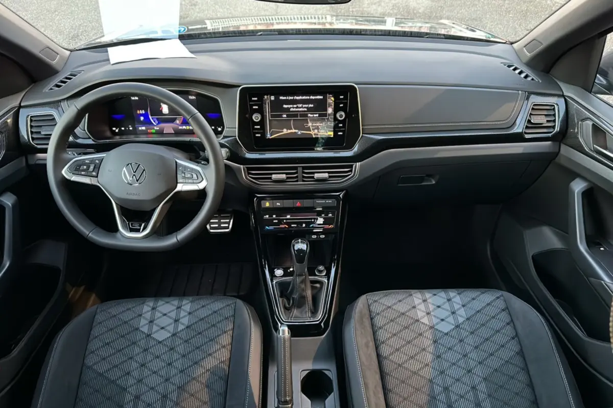 Vue intérieure avant du Volkswagen T-Cross TSI 116 DSG7 R-Line 2025 avec tableau de bord numérique et sellerie tissu grise.