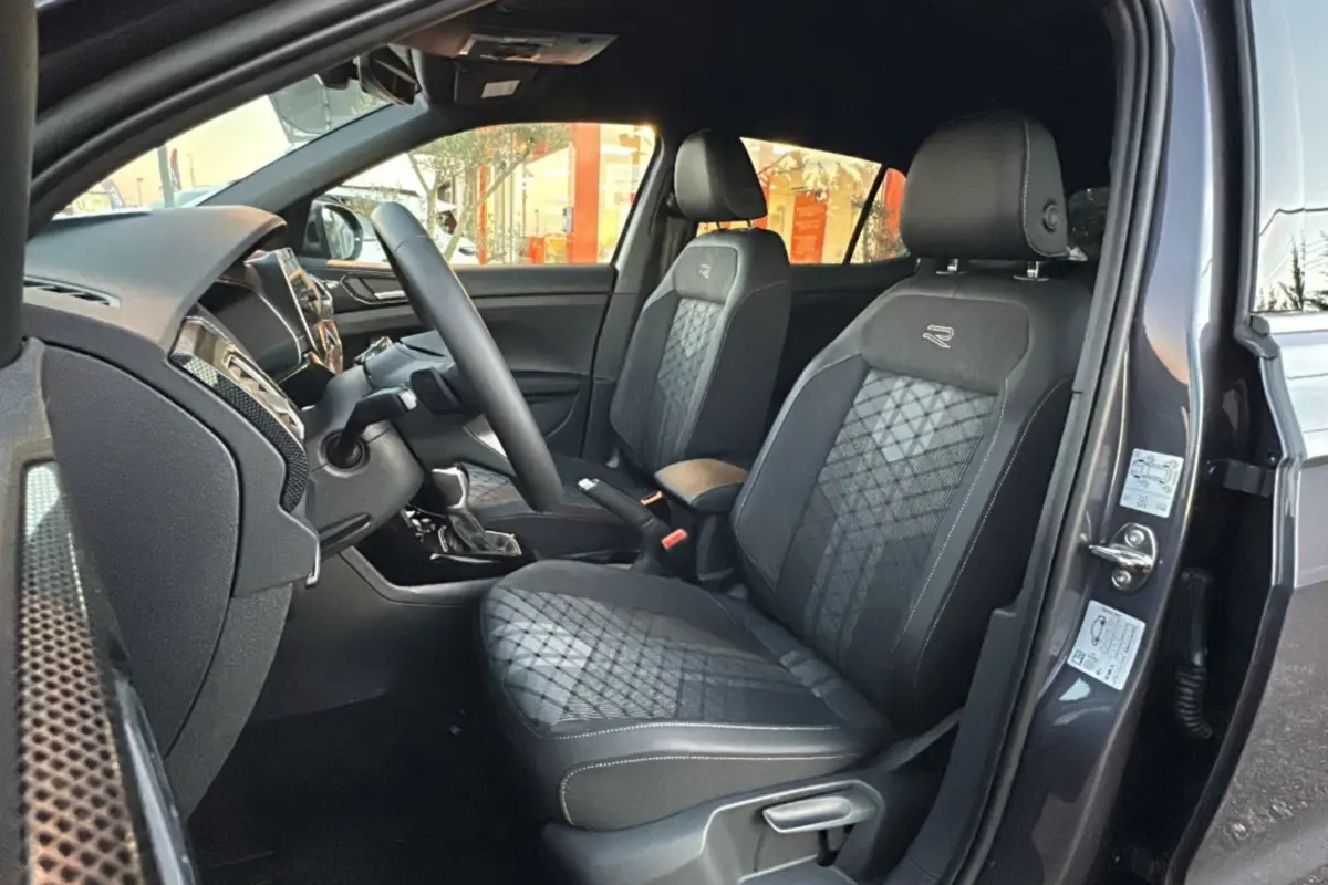 Intérieur avant du Volkswagen T-Cross gris cendré 2025, sièges tissu R-Line avec surpiqûres et volant multifonctions cuir.