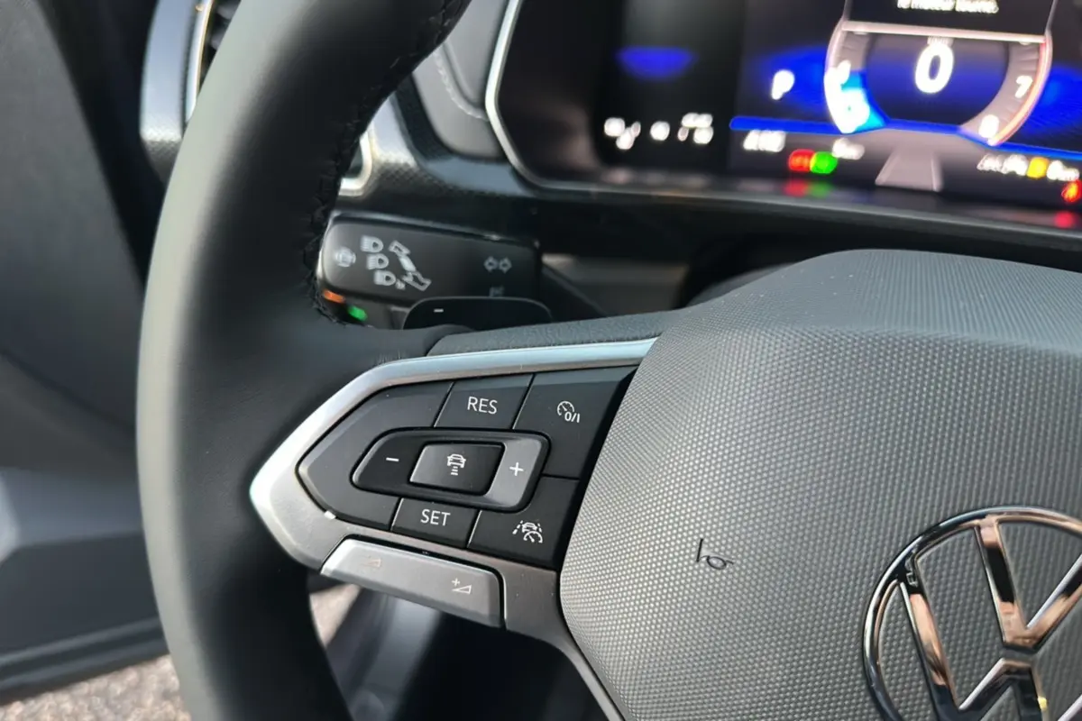Gros plan sur le volant cuir multifonctions gris d’un Volkswagen T-Cross 2025 avec commandes de régulateur adaptatif.