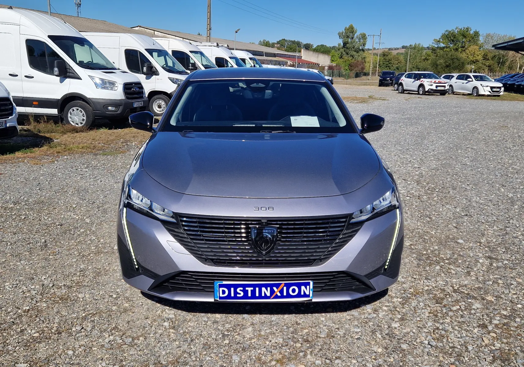 Vue avant d'une Peugeot 308 1.2 Hybrid 145 gris Artense avec calandre noire et feux LED verticaux allumés.