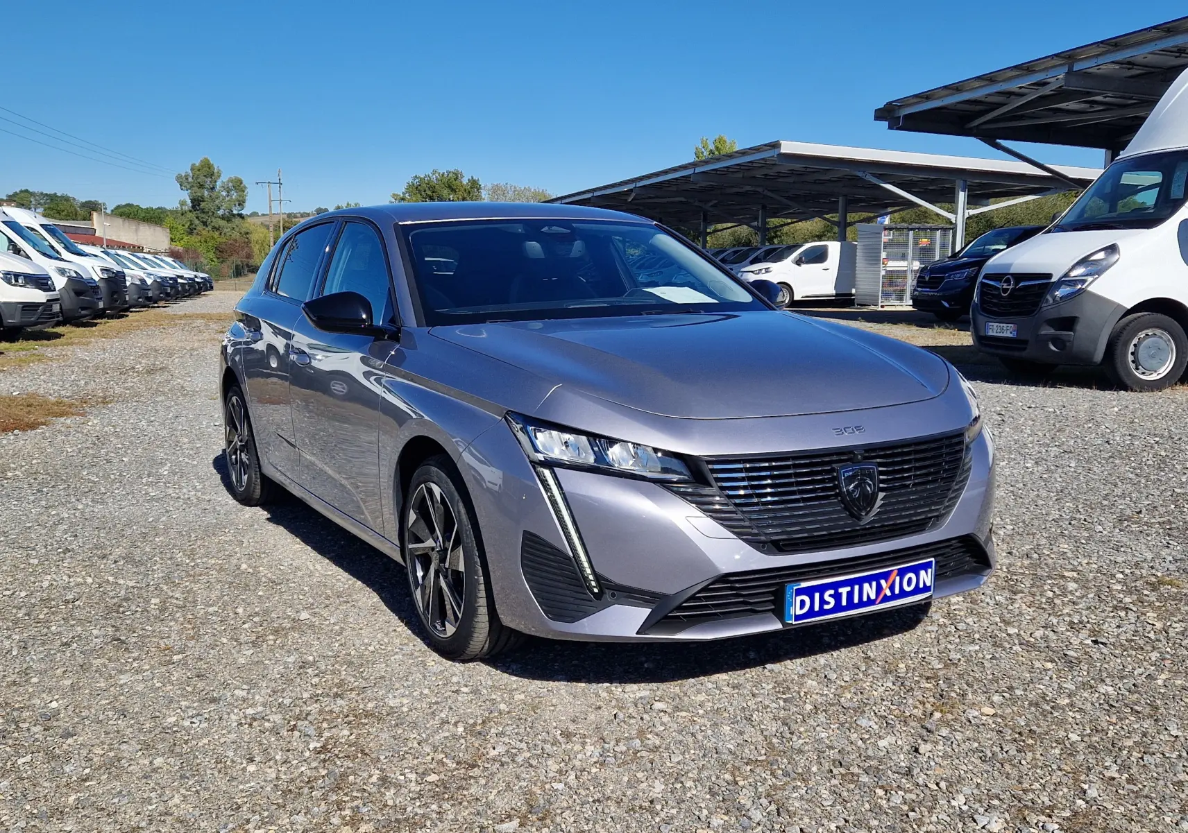 Peugeot 308 gris Artense vue 3/4 avant droit, avec calandre noire distinctive et jantes alliage noires.