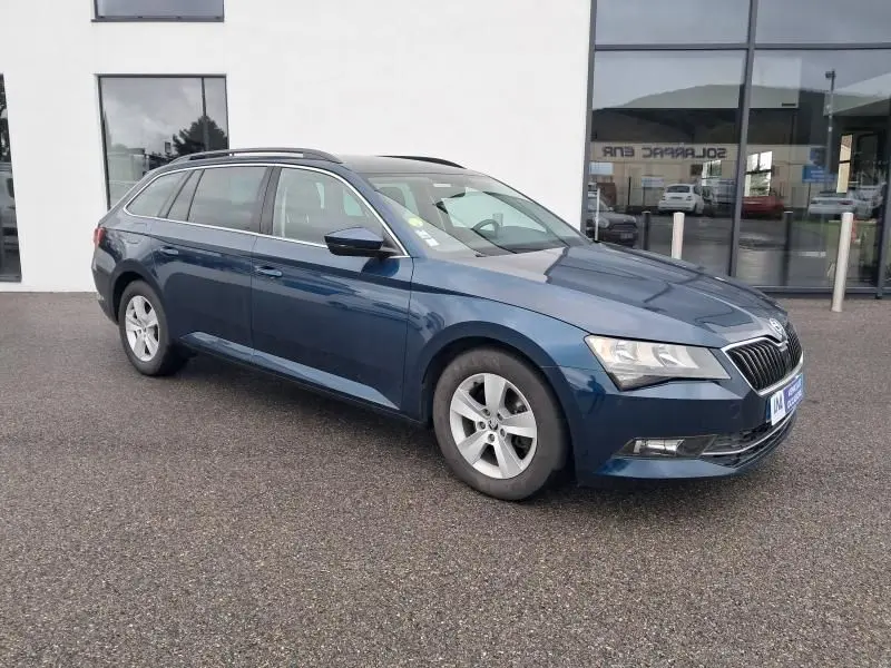 Vue 3/4 avant droite d'une Skoda Superb Combi bleu métal de 2018 stationnée devant un bâtiment vitré.